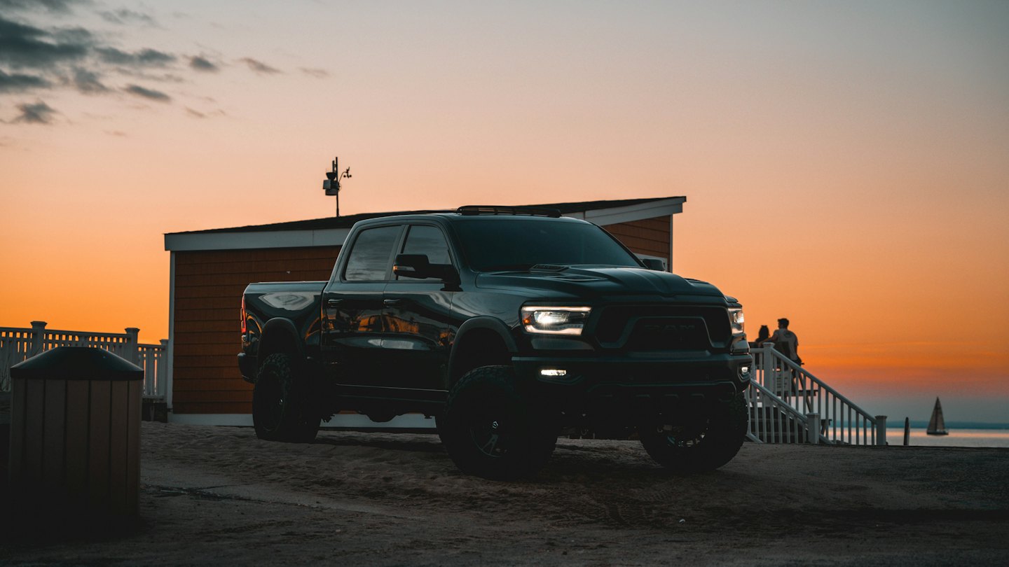 Black pickup truck parked on sand with headlights glowing.