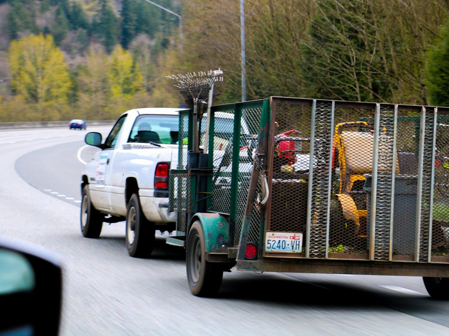 White pickup truck tows landscaping trailer on highway.