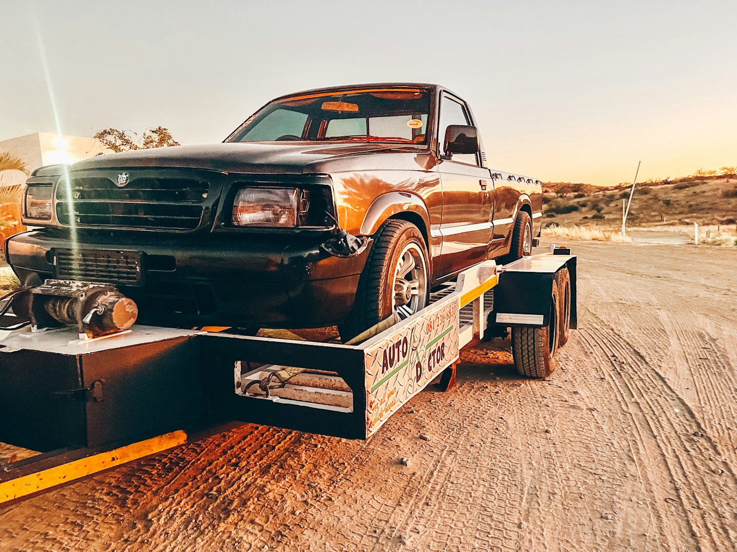 Brown pickup truck on a flatbed trailer on a dusty road.