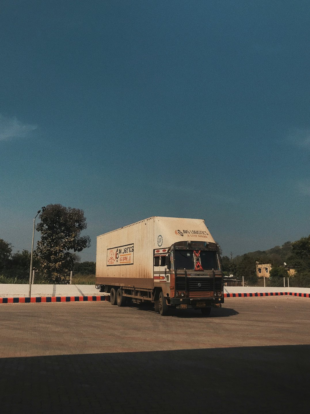 Cargo truck parked on a paved lot near green hills.